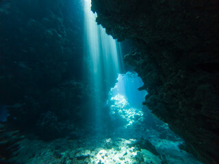 Landscape view of sunlight sunbeams dancing from the surface in underwater sea cave with rock walls