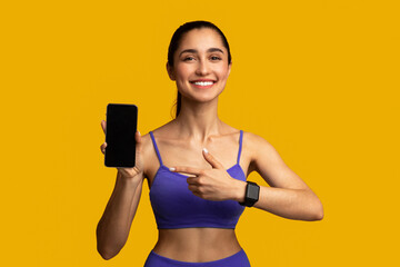 Sports Application. Cheerful smiling fit young lady holding and showing cellphone with black empty...