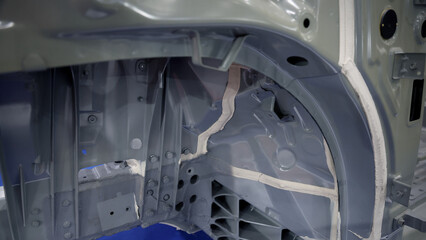 Car body frame. Automotive chassis and interior body frame. Visible weld seams sealant applications and vibration damping sheets. Vehicle chassis structural reinforcement and manufacture precision.