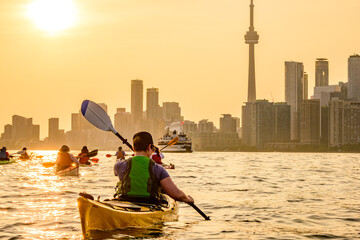 Group of kayakers paddling  into the setting sun and toward the downtown city skyline shot in toronto in summer room for text copy space