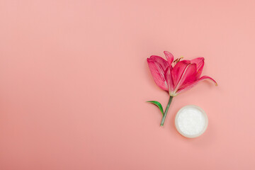 Skincare cosmetics concept with red lily on soft pink background, flat lay. Natural selfcare