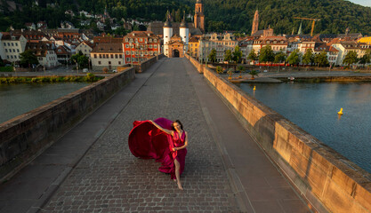 junge Frau in rotem Kleid, tanzt in der Morgensonne, über die alte Brücke in Heidelberg.