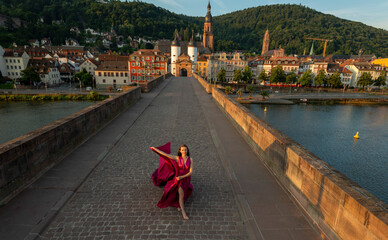 junge Frau in rotem Kleid, tanzt in der Morgensonne, über die alte Brücke in Heidelberg.