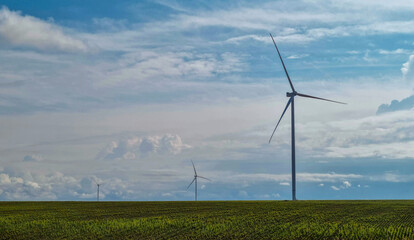 Wind turbines rotating on green agricultural field under cloudy blue sky. Landscape with modern...