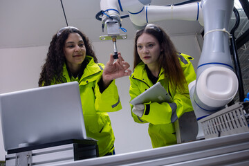 Women engineers collaborating with a robotic arm in a modern workspace environment