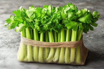 Fresh green celery stalks in burlap bag on gray surface