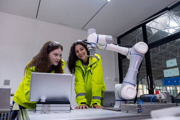 Two students explore robotics technology while collaborating with a robotic arm in a modern lab setting during the day