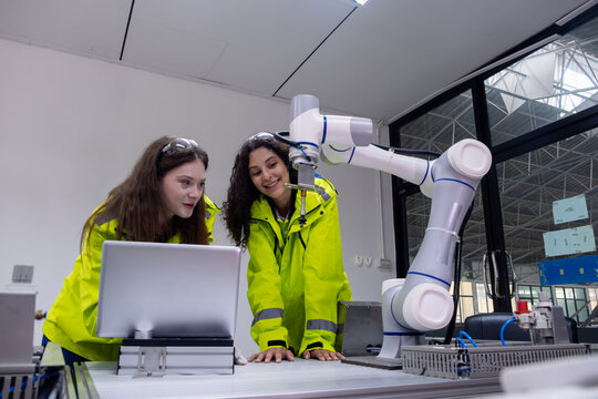 Two students explore robotics technology while collaborating with a robotic arm in a modern lab setting during the day