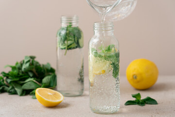 Water Pouring into Glass Bottle with Detox Drink: Fresh Lemon, Cucumber, and Mint Infused Beverage