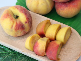 A ripe peach on a rustic wooden plate decorated with green palm leaves, tropical and natural still life composition, close-up.