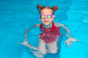 Cute little child girl learning to swim in the pool, wearing goggles. Childhood and development of children sport. Strengthening baby's health. Healthy activity for children. High quality photo