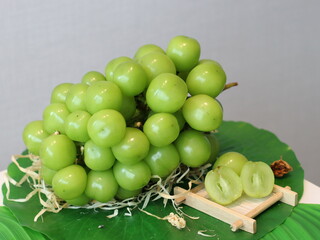 A bunch of fresh grapes on a rustic wooden plate decorated with green palm leaves, tropical and natural still life composition, close-up.