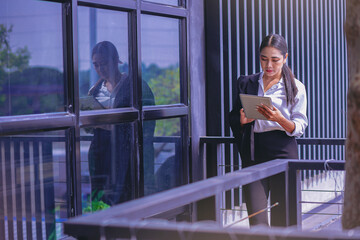 Working woman with touchpad, relaxing outside office building.