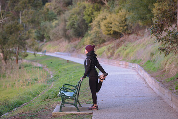 Woman warming up on a footpath next to a park bench before jogging, Lake Colac, Victoria, Australia
