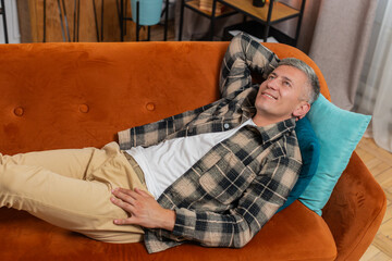 Tired young man with gray hair sitting on comfortable couch, taking a rest, daytime nap. Portrait...