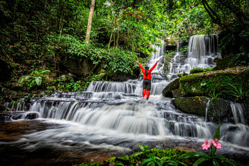 Majestic Waterfall View, A traveler standing triumphantly on a rock near a stunning wide waterfall,...