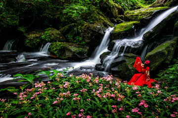 Spectacular view of the waterfall. Tourists in bright red costumes sit on rocks near the impressive...