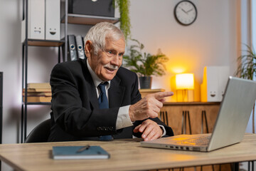 Senior businessman working on laptop computer at home office desk talk on online communication video call with employee, boss. Grandfather manager freelancer guy support services looking at webcam.