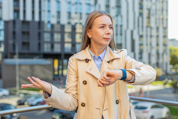 Upset mature woman standing outside office looking around waiting for business meeting impatient...