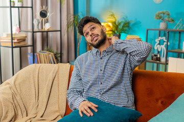 Tired ill sick Indian young man suffers from spine neck muscle discomfort pain. Exhausted Hispanic...