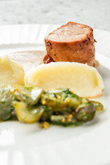 Sliced pork tenderloin with creamy mashed potatoes, brown sauce, and pickled cucumbers with herbs,...