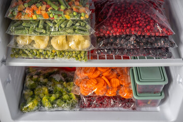 Plastic bags with different frozen vegetables and berries in refrigerator.  Winter supply food in zip bags, preserving nutrients. Vegetables on the freezer shelves.