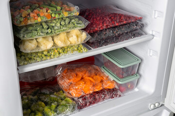 Plastic bags with different frozen vegetables and berries in refrigerator.  Winter supply food in zip bags, preserving nutrients. Vegetables on the freezer shelves.