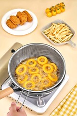 Delicious Onion Rings Frying in a Stainless Steel Mesh Basket on a Stovetop, Fried onion rings in a...