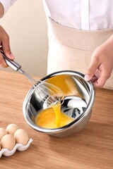 Whisking Eggs in Stainless Steel Bowl Baking Preparation, Man whisking eggs in metal bowl on wooden table, closeup