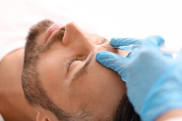 Closeup of bearded man getting beauty injection in clinic. Cosmetologist hands in blue rubber...