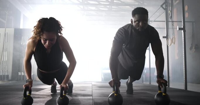 Diverse workout partners completing kettlebell push-up reps at gym celebrating set with high-five