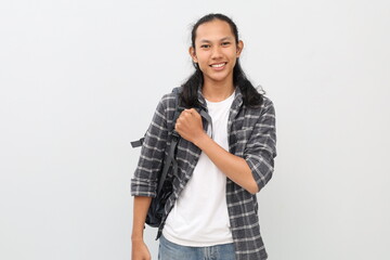 Young asian male student wearing casual clothes and backpack, celebrating victory or feeling proud while clenching fists on chest, standing smiling looking at camera, isolated white background.