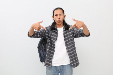 Photo of young male student wearing casual clothes and backpack, shouting while pointing down at empty space, standing looking at camera, isolated on white background.