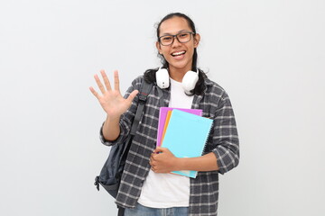 Handsome asian student man wearing casual clothes, glasses, backpack, headphones around neck and carrying books, counting five with fingers, standing isolated on white background.