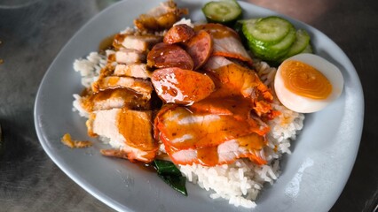 Red pork and crispy pork on rice in a blue plate on a table