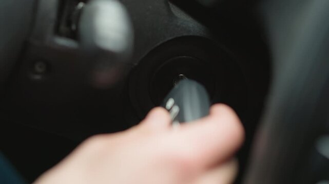 Close up of urban explorer inserting metal key into ignition starter and turning key inside vehicle cabin focusing on hand movement dashboard blur and winter jacket sleeve before engine start signal