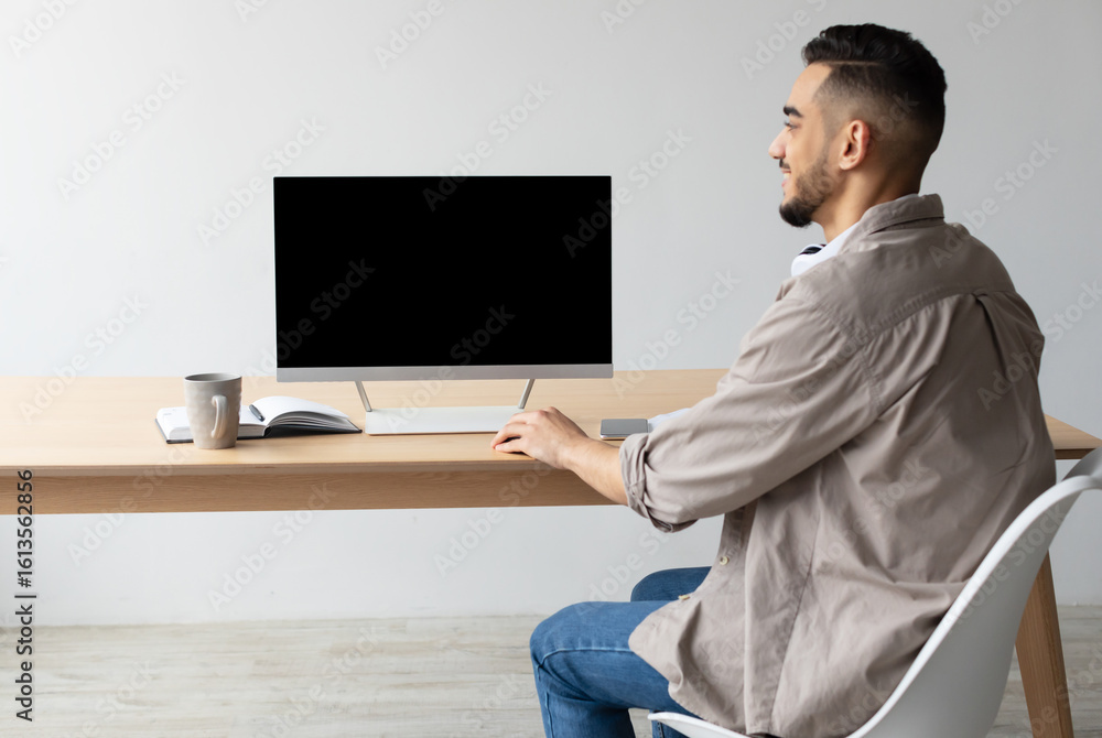 Poster rear back view of happy middle eastern man looking at blank empty computer monitor sitting at desk a