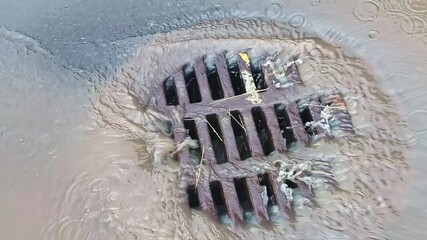 Iron street drain grate with dirty stormwater flowing during rainfall in urban area