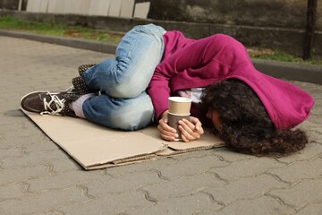 Homeless woman with paper cups lying on carton outdoors
