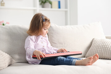 Obraz premium Cute little girl playing toy electric piano on sofa at home