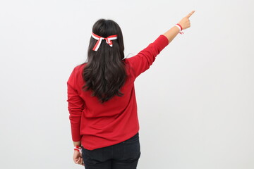 Indonesian woman celebrating the independence day of the Republic of Indonesia, pointing upwards in empty space, standing back view, isolated on white background.