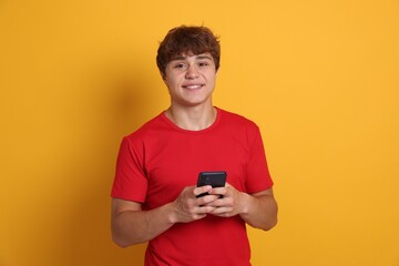 Fototapeta premium Portrait of smiling teenage boy with smartphone on yellow background