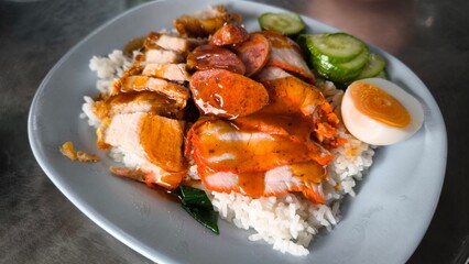 Red pork and crispy pork on rice in a blue plate on a   table in Thailand