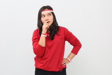 Indonesian woman with red and white ribbon to celebrate Indonesian independence day standing looking up in empty space, touching lips, thinking something.