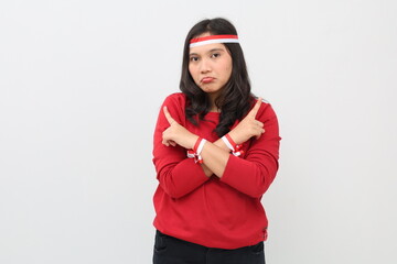Indonesian woman confused with red and white ribbon to celebrate Indonesian independence day standing with crossed arms pointing right and left with fingers, two choices.