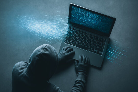 Digital Threat: A hooded figure hunches over a laptop, the machine glowing with a web of energy, symbolizing a potential security breach or the creation of digital technology. 