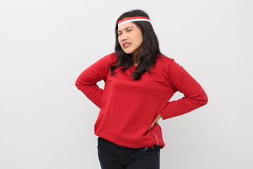 Indonesian woman with red and white ribbon celebrating Indonesian independence day while having back pain, standing isolated on white background.