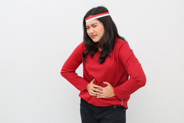 Indonesian woman with red and white ribbon celebrating Indonesian independence day standing holding stomach, stomach ache concept, standing isolated on white background.