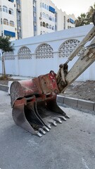 Malaga, Spain - July 25, 2025: Excavator bucket with detailed teeth positioned on construction site near residential buildings and decorative wall