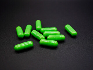 A group of green capsules arranged on a black background. The glossy texture and bright green color of the pills stand out against the matte surface, creating a clean and professional pharmaceutical 